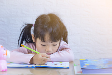 Cute little girl doing homework, reading a book, coloring pages, writing and painting. Children paint. Kids draw. Preschooler with books at home. Preschoolers learn to write and read. Creative toddler