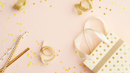 Children birthday party concept. Top view bag with gifts, party serpentine and golden confetti on beige table.