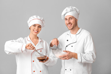 Canvas Print - Young confectioners cooking tasty desserts on grey background