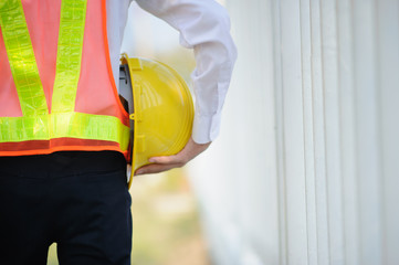 Engineer holding yellow helmet safety hard hat construction background