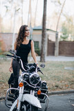 Fototapeta Miasto - Young beautiful biker woman in a black tank top and leather pants on a motorcycle. The concept of speed and freedom. Soft selective focus.