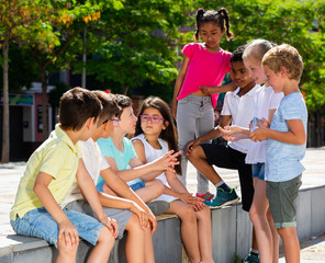 Wall Mural - Group of cheerful  children sitting on bench and sharing secrets