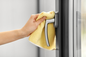 hygiene, household and cleanliness concept - close up of female hand cleaning window handle with microfiber rag