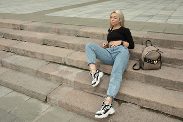 Wall Mural - Young attractive female blonde in jeans sitting on stone stairs.