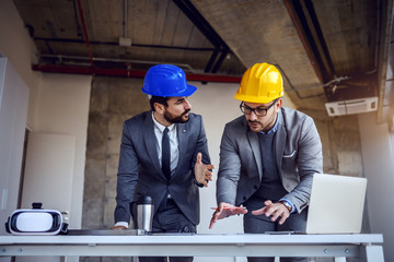 Wall Mural - Two dedicated hardworking architects standing in building in construction process and working on improvement of blueprints.