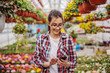© Dusan Petkovic - Young smiling female entrepreneur standing at hothouse and taking orders online. Hothouse interior.
