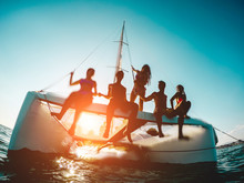 Silhouette Of Young Friends Chilling In Private Catamaran Boat - Group Of People Making Sea Tour Trip - Alternative Travel Vacation During Coronavirus Outbreak - Focus On Left Girl - Water On Camera