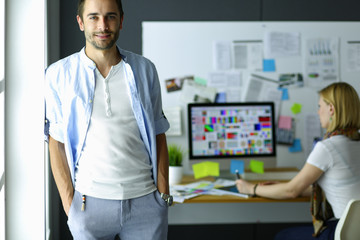 Poster - Portrait of young designer in front of laptop and computer while working. Assistant using her mobile at background.