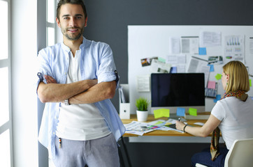 Poster - Portrait of young designer in front of laptop and computer while working. Assistant using her mobile at background.