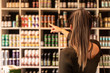 A young woman pointing at some canned beers in a liquor shop and choosing. Beers from trendy small breweries displayed on shelfs. Bokeh background