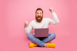 Full length photo excited delighted guy sit floor legs crossed folded work computer celebrate online lottery win raise fists scream yes wear white jumper jeans isolated pastel color background