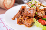 Fototapeta Kuchnia - Spicy pork minced with tomatoes and lettuce on a white plate on a wooden table.