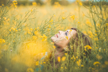 Sticker - beautiful romantic girl sitting on blooming rapeseed field enjoying nature, young elegant woman walking, pretty female face looking up from flowers