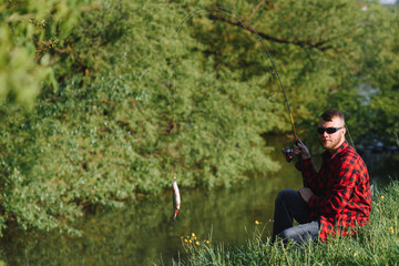 Wall Mural - Fisher man fishing with spinning rod on a river bank, spin fishing, prey fishing