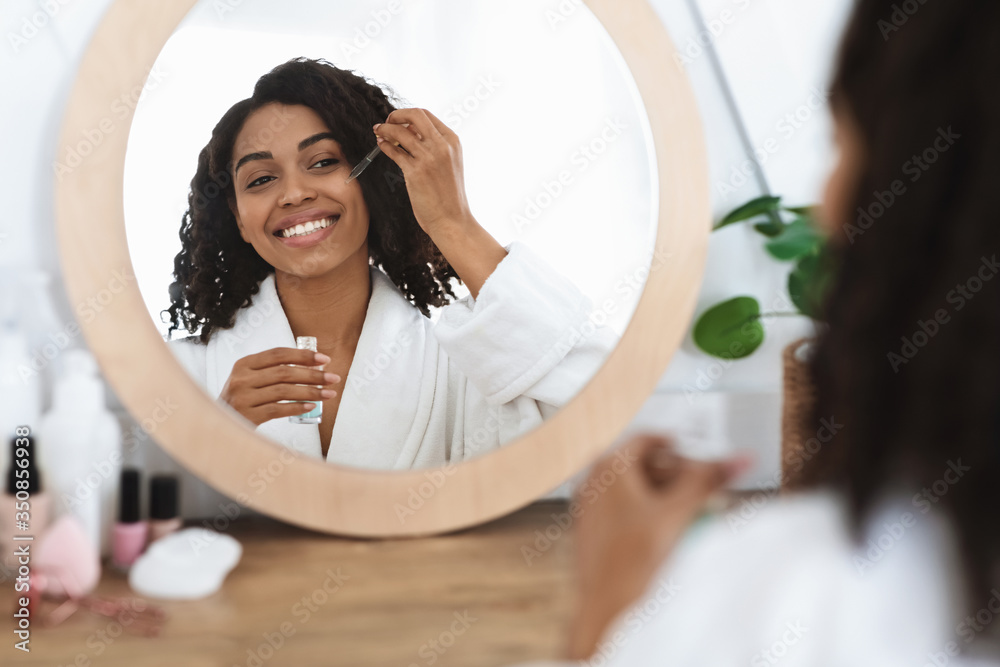 Skin nutrition. Beautiful black woman applying moisturizing serum on face at home - obrazy, fototapety, plakaty 