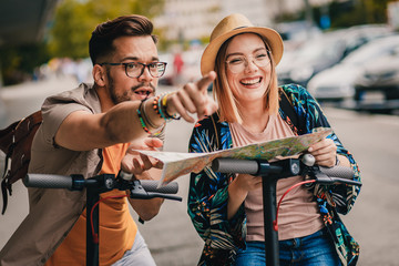 Wall Mural - Young couple on vacation having fun driving electric scooter through the city, they looking at map for direction.