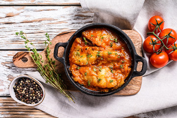 Tilapia fish baked in tomatoes in a pan. White wooden background. Top view