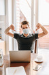 © LIGHTFIELD STUDIOS - young man in medical mask showing thumbs down near laptop and cup of coffee on table