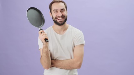 Sticker - A handsome young man wearing a white t-shirt is holding a frying pan standing isolated over gray background