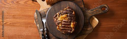 Fotografía top view of tasty grilled steak served on wooden board near cutlery, panoramic s