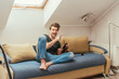 © LIGHTFIELD STUDIOS - excited young man pointing with finger while knitting on sofa at home