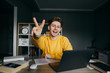 © bodnarphoto - A good positive student studies at home with books and the Internet on a laptop, poses for the camera with a happy face and shows a gesture of peace to the camera. Distance learning at home on desktop