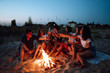 © maxbelchenko - Group of friends near a campfire on the beach cheers and drinking beer at night. Summer holidays, vacation, relax and lifestyle concept.
