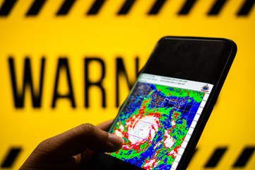 mobile phone logged into photo of cyclone with warning background