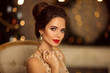 © Victoria Andreas - Beauty portrait of elegant woman with wedding hairstyle and makeup. Beautiful brunette girl with golden jewelry in prom dress sitting on modern chair over bokeh lights xmas decorations.