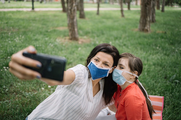 Portrait of girl and woman wearing masks in park. Woman and girl wearing medical masks and taking selfie while sitting in forest.