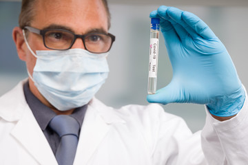 Scientist or doctor with medical face mask and medical gloves is handling virus test tube with result markers in front of laboratory in background