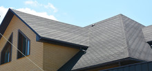 A Close-up On A Roof Problem Area Covered With Asphalt Roof Shingles And Irregular Shape Window On The Wall Of The House Construction.