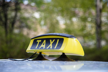 Close-up of taxi sign on a car on a blurred background of green trees