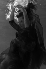  Black and white photo. Beautiful girl underwater in a red dress swims in the pool. Tenderness and elegance. Bubbles and a lot of water