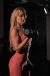 © Михаил Решетников - European woman blonde with a sports figure wearing gloves does biceps exercise with dumbbell. Fitness bikini model posing in the gym. Female bodybuilder.
