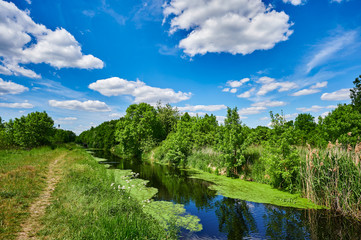 blue and cloudy sky over a little creek in the surrounding countryside of berlin, germany.
