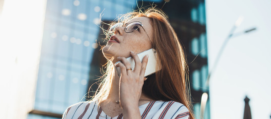 Red haired caucasian woman with freckles looking up through eyeglasses while talking on phone