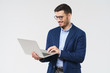 © Damir Khabirov - Young modern businessman wearing blue blazer and casual shirt, standing with open laptop in hands, browsing websites with smile, isolated on gray background