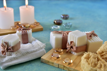 Spa and relaxation concept. Bath and aromatherapy accessories in natural wood craft table, handmade soap, sea sponge, towel, lighted candles and glass gems. White, water blue, beige colors.