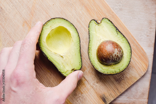 Fotomural Mano cogiendo aguacate cortado por la mitad sobre un fondo de madera
