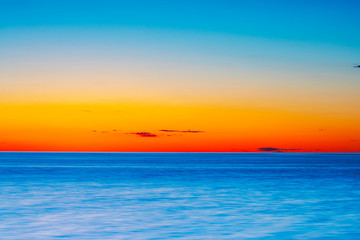 Wall Mural - Vibrant colored summer sunset reflecting in ocean with endless horizon and deep blue ocean at island of Gotland in Sweden