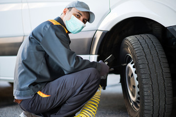 Poster - Masked mechanic checking the pressure of a van tire