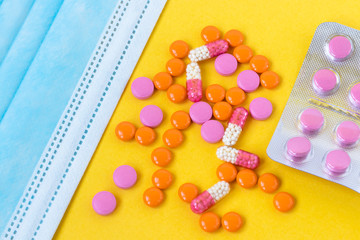 Multi-colored pills and a blue disposable mask on a bright yellow background, top view. Medication for the disease. Drugs from coronavirus virus disease and vitamins for health. Close up. Copy space.