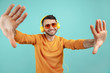 © Screaghin - Careless bearded young man wearing sunglasses listening to music and dancing on cyan background.