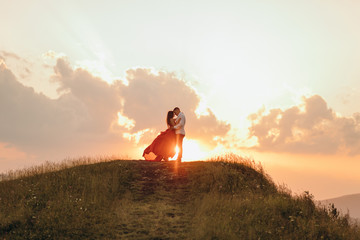 Happy couple stands in embrace and kisses each other on beautiful sunset in mountain.