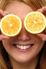 A woman with a smile using two slices of orange to cover her eyes