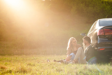 Beautiful young couple having fun at sunset near car