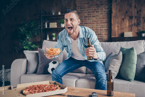 Photo of domestic handsome guy stay home quarantine time watch television eat pizza drink beer sit cozy sofa football season opening support favorite team modern interior living room indoors