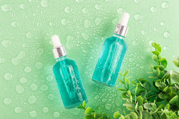 Poster - Moisturizing beauty essence in a dropper glass bottle on green background with water drops. Spa bathroom concept, copy space for your text