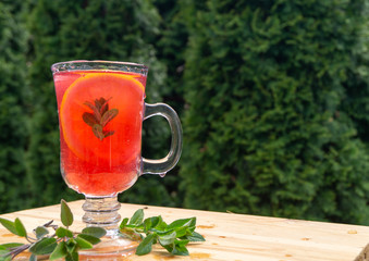 Wall Mural - glass goblet with cold cocktail on a wooden table in the garden on a background of green plants